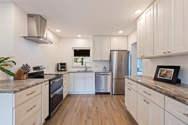 kitchen featuring white cabinets, wall chimney exhaust hood, light stone counters, stainless steel appliances, and a sink