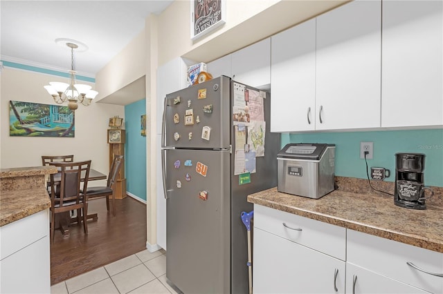 kitchen with light tile patterned flooring, an inviting chandelier, decorative light fixtures, stainless steel refrigerator, and white cabinets