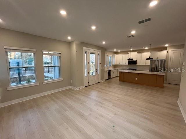 kitchen featuring pendant lighting, appliances with stainless steel finishes, white cabinetry, a kitchen island, and light wood-type flooring