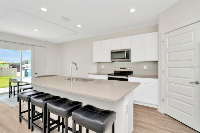 kitchen featuring appliances with stainless steel finishes, white cabinetry, sink, a breakfast bar area, and a center island with sink