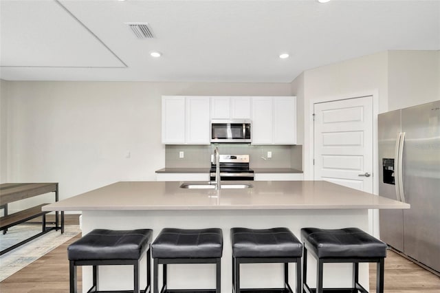 kitchen featuring tasteful backsplash, an island with sink, sink, white cabinets, and stainless steel appliances