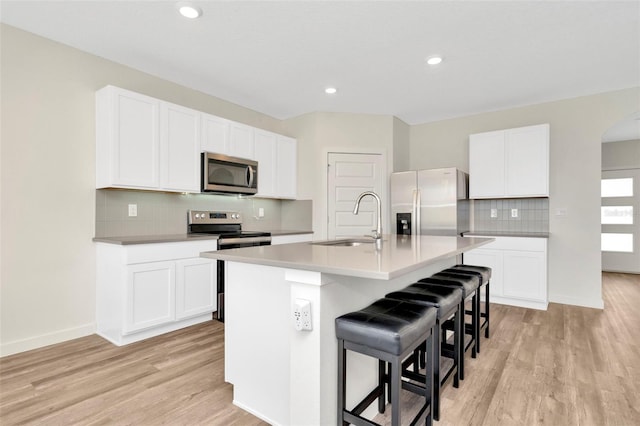 kitchen featuring a breakfast bar, sink, a center island with sink, appliances with stainless steel finishes, and white cabinets