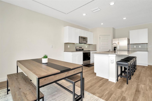 kitchen featuring a kitchen breakfast bar, a kitchen island with sink, stainless steel appliances, light hardwood / wood-style floors, and white cabinets