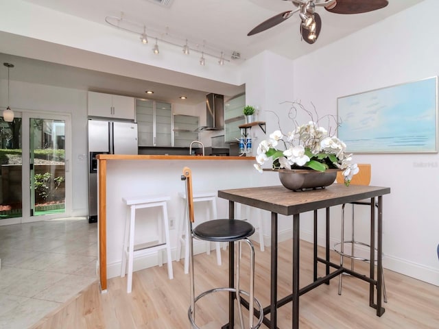 kitchen with light hardwood / wood-style flooring, stainless steel refrigerator with ice dispenser, decorative light fixtures, kitchen peninsula, and wall chimney exhaust hood