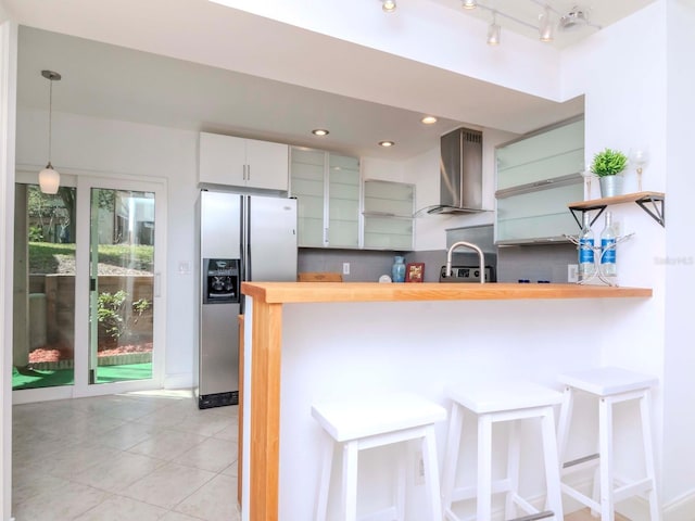 kitchen with wall chimney exhaust hood, a breakfast bar, decorative light fixtures, stainless steel fridge with ice dispenser, and kitchen peninsula