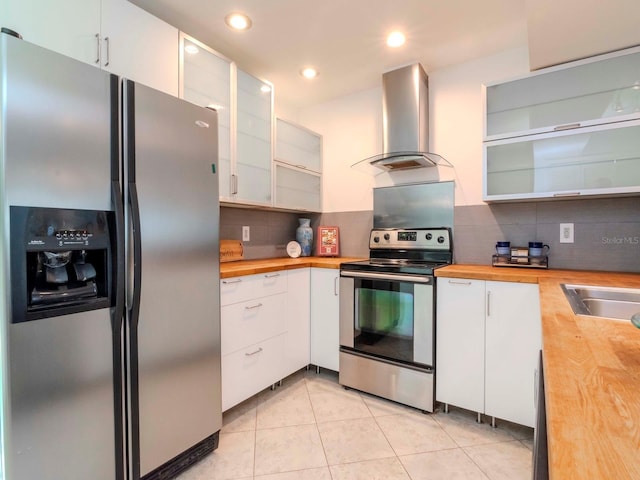 kitchen with butcher block countertops, white cabinetry, ventilation hood, light tile patterned floors, and stainless steel appliances