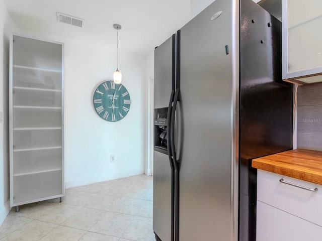 kitchen with stainless steel refrigerator with ice dispenser, light tile patterned floors, wooden counters, and decorative light fixtures