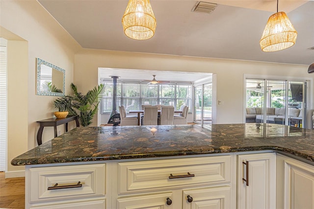 kitchen featuring pendant lighting, a healthy amount of sunlight, dark stone counters, and white cabinets