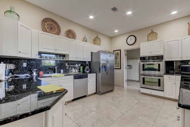 kitchen with stainless steel appliances, white cabinets, backsplash, and dark stone counters