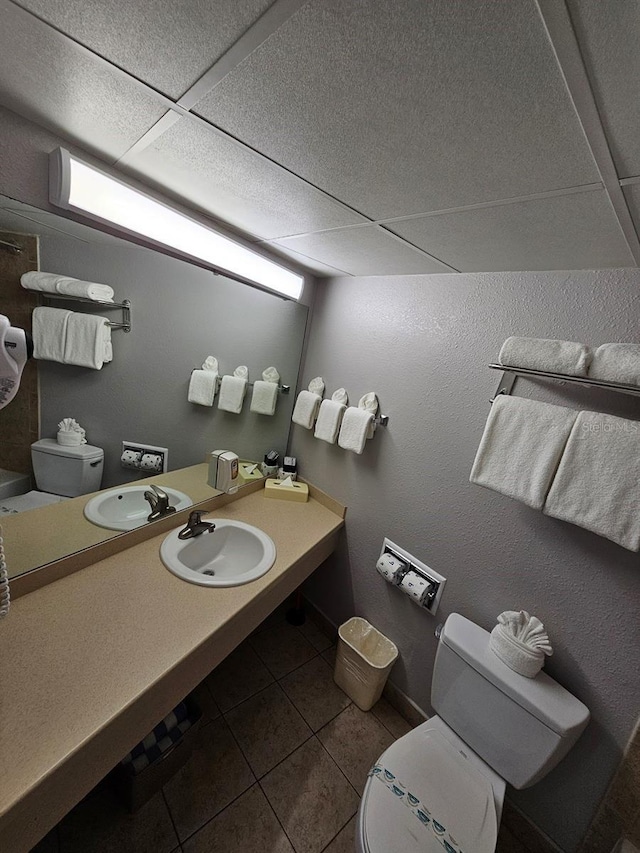 bathroom with a paneled ceiling, toilet, tile patterned flooring, and sink