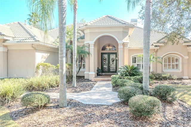 view of exterior entry with a tiled roof, stucco siding, french doors, and a chimney