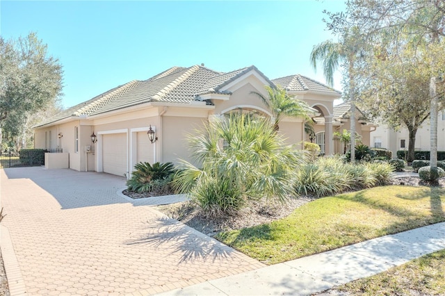 view of front of house with decorative driveway, stucco siding, an attached garage, and a tiled roof