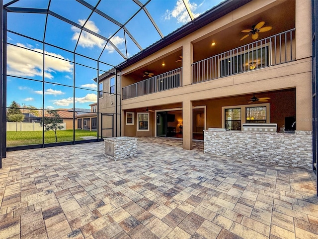 back of property featuring a bar, an outdoor kitchen, a lanai, ceiling fan, and a patio area