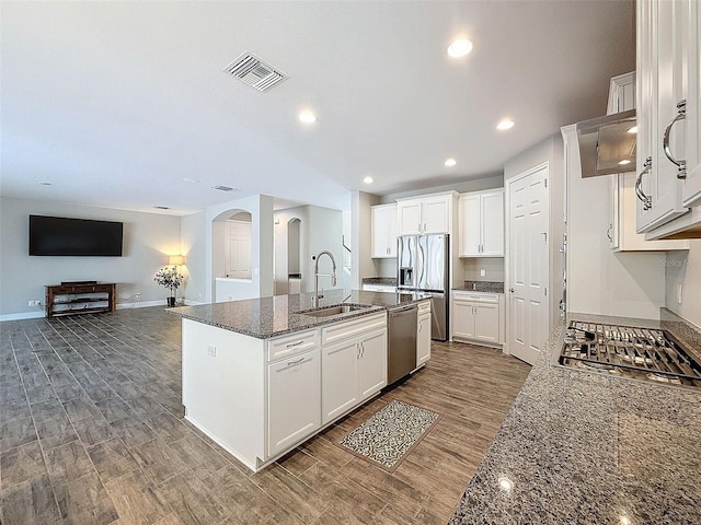 kitchen featuring sink, appliances with stainless steel finishes, a kitchen island with sink, white cabinets, and dark stone counters