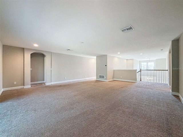 spare room with light carpet, visible vents, arched walkways, and baseboards