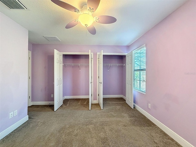 unfurnished bedroom featuring ceiling fan, a textured ceiling, carpet floors, and multiple closets