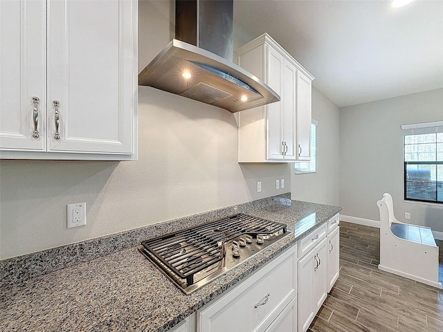 kitchen featuring baseboards, wood tiled floor, stainless steel gas stovetop, white cabinetry, and wall chimney exhaust hood