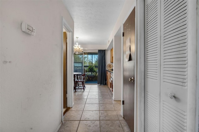 hall with a notable chandelier, a textured ceiling, and light tile patterned flooring