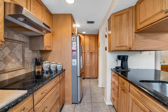 kitchen with light tile patterned flooring, black electric cooktop, stainless steel fridge, dark stone counters, and decorative backsplash