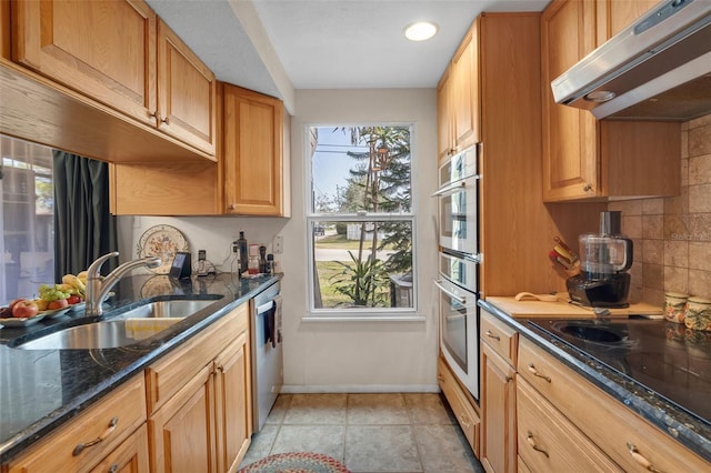 kitchen with sink, light tile patterned floors, appliances with stainless steel finishes, dark stone countertops, and backsplash