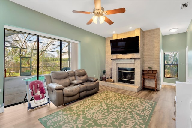 living room with ceiling fan, a brick fireplace, and light wood-type flooring