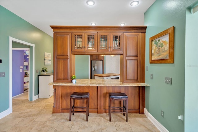 kitchen with stainless steel fridge with ice dispenser, light stone counters, a breakfast bar, and kitchen peninsula