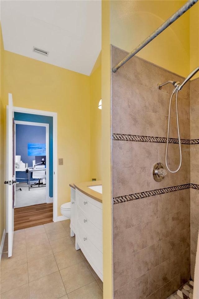 bathroom with lofted ceiling, tile patterned flooring, vanity, tiled shower, and toilet