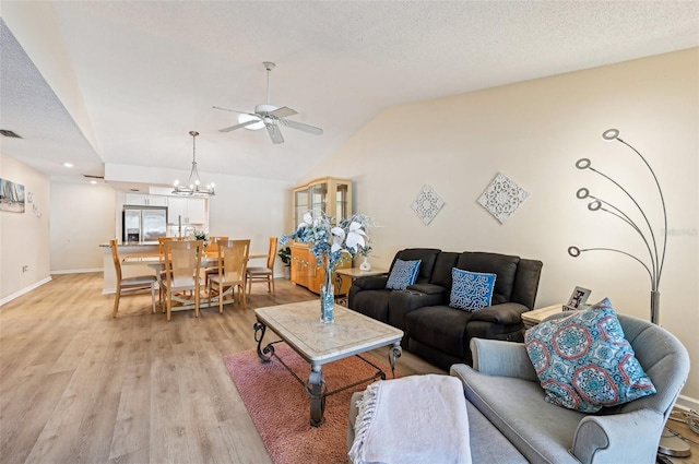 living room featuring vaulted ceiling, ceiling fan with notable chandelier, a textured ceiling, and light wood-type flooring