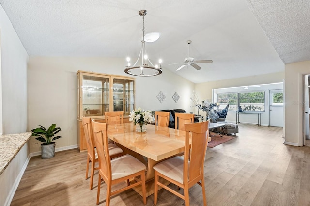 dining room featuring lofted ceiling, ceiling fan with notable chandelier, light hardwood / wood-style floors, and a textured ceiling