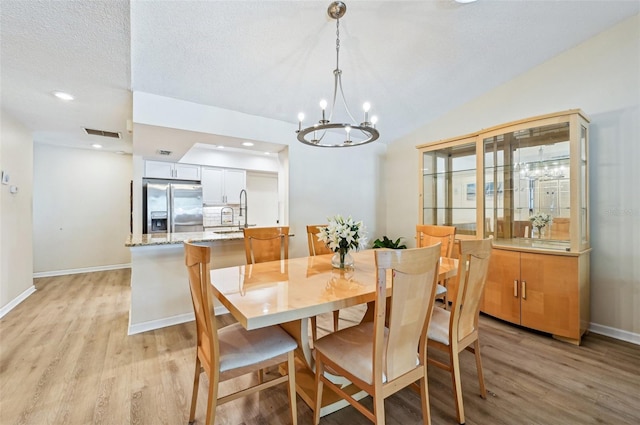 dining space with a notable chandelier, vaulted ceiling, a textured ceiling, and light wood-type flooring