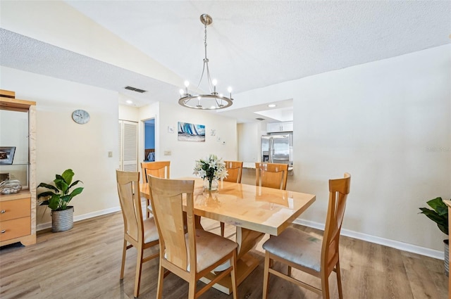 dining area with vaulted ceiling, light hardwood / wood-style flooring, and a textured ceiling