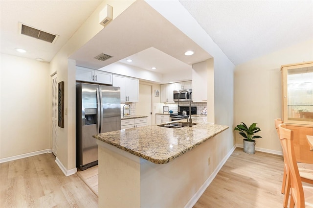 kitchen with white cabinets, kitchen peninsula, stone counters, stainless steel appliances, and backsplash