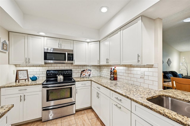 kitchen featuring white cabinetry, appliances with stainless steel finishes, backsplash, and light stone counters