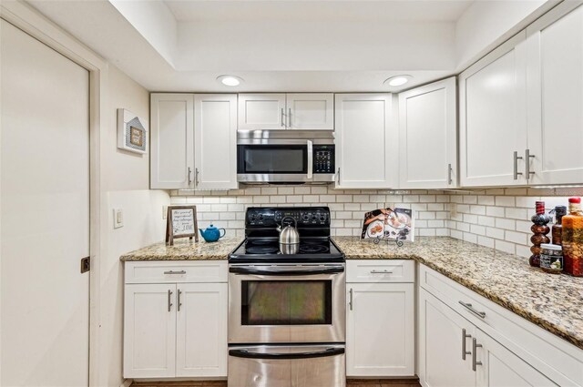 kitchen with tasteful backsplash, appliances with stainless steel finishes, white cabinets, and light stone counters