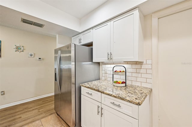 kitchen with white cabinetry, stainless steel fridge, decorative backsplash, light hardwood / wood-style floors, and light stone counters