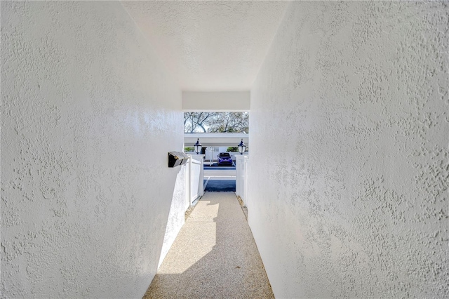 hall with light colored carpet and a textured ceiling