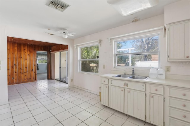 kitchen featuring wooden walls, white cabinetry, sink, light tile patterned floors, and ceiling fan