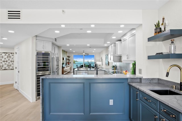 4951 Bacopa Ln S Unit 103, Saint Petersburg, FL 33715 - kitchen featuring wall chimney exhaust hood, blue cabinets, sink, white cabinetry, and kitchen peninsula