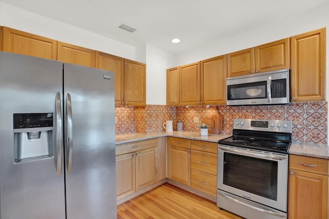 kitchen featuring tasteful backsplash, stainless steel appliances, light stone countertops, and light wood-type flooring