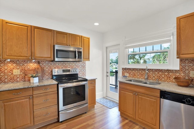 kitchen featuring sink, backsplash, stainless steel appliances, light stone countertops, and light wood-type flooring