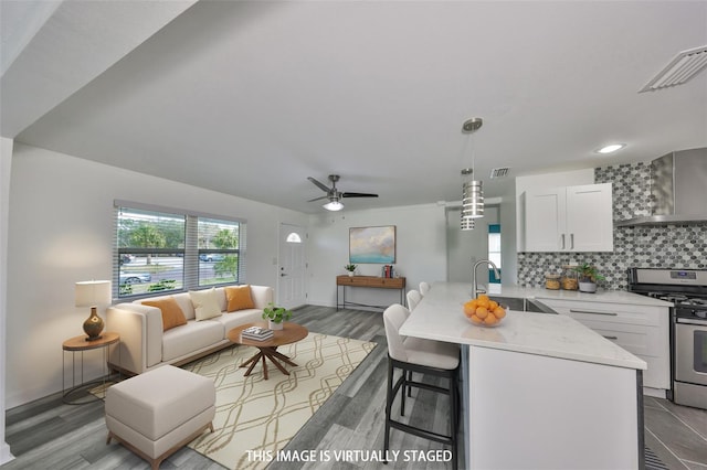 kitchen with pendant lighting, sink, white cabinets, gas range, and wall chimney exhaust hood