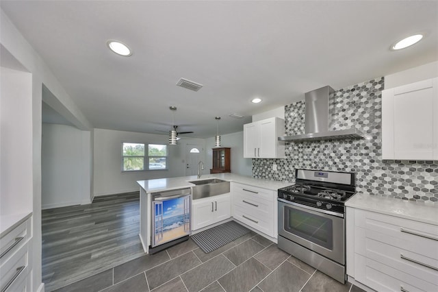 kitchen featuring sink, gas range, white cabinetry, kitchen peninsula, and wall chimney range hood