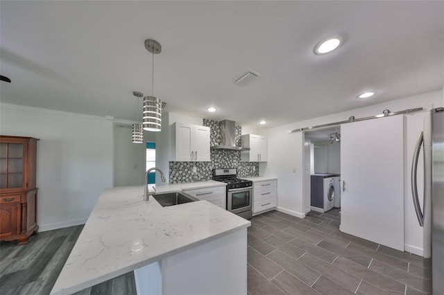 kitchen with white cabinetry, hanging light fixtures, stainless steel appliances, a barn door, and wall chimney exhaust hood