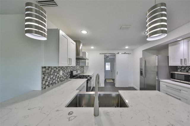 kitchen with sink, appliances with stainless steel finishes, light stone countertops, a barn door, and wall chimney exhaust hood