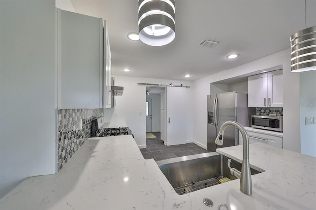 kitchen with sink, decorative backsplash, light stone counters, stainless steel appliances, and a barn door