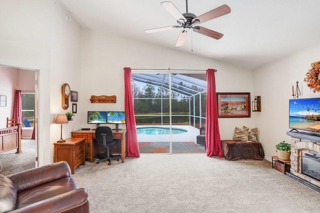 office space featuring a sunroom, carpet flooring, vaulted ceiling, a stone fireplace, and ceiling fan