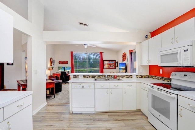 kitchen featuring white appliances, lofted ceiling, a peninsula, light countertops, and a sink