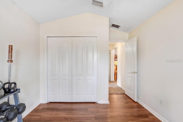 unfurnished bedroom featuring wood finished floors, visible vents, baseboards, vaulted ceiling, and a closet