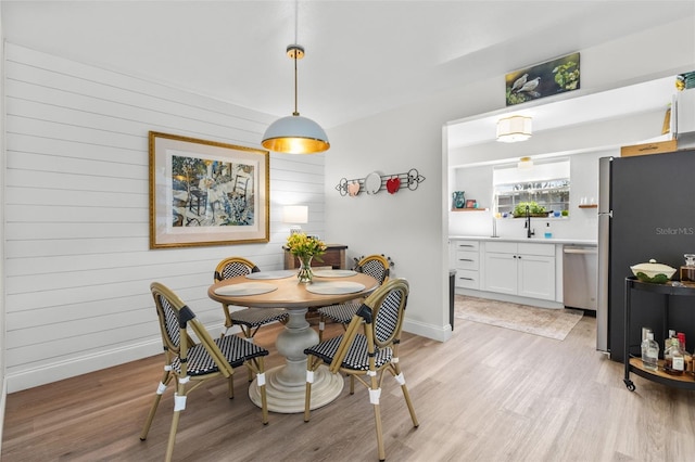 dining space with sink, light hardwood / wood-style flooring, and wood walls