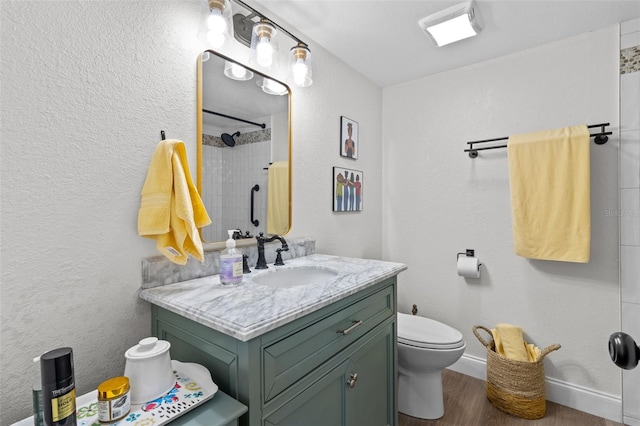 bathroom featuring vanity, wood-type flooring, a tile shower, and toilet